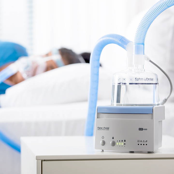 女性患者がF&P 820熱線入り呼吸回路に接続されたNIVマスクを装着しベッドで眠っている様子